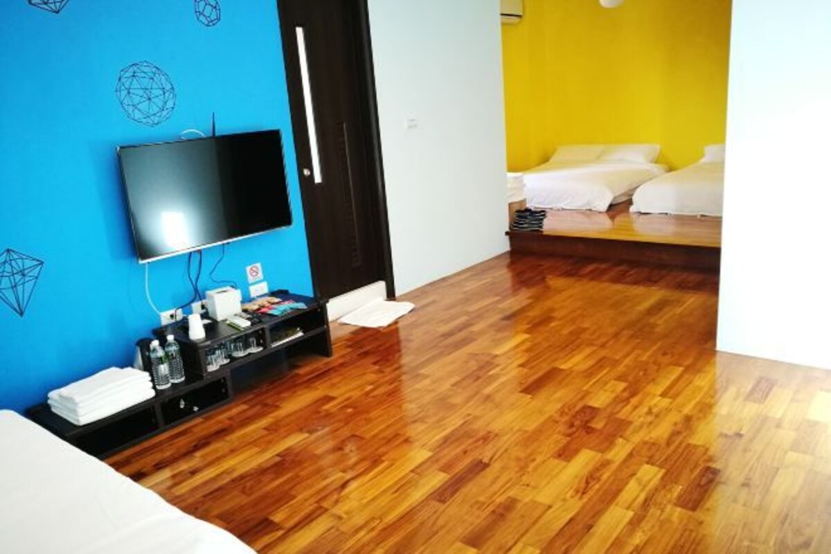 A hotel room with a wooden floor, a TV mounted on the wall, a bed with white bedding, and a small shelf with toiletries.
