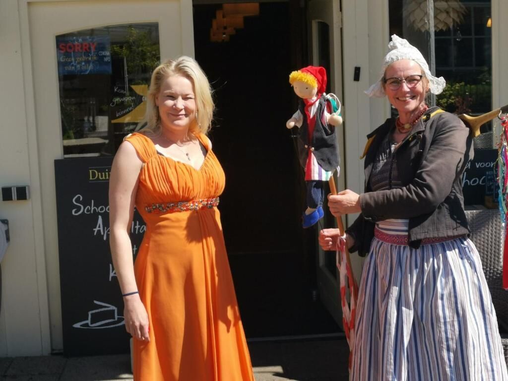 Twee personen staan buiten een gebouw met een bord waarop 'Sorry' en 'School' staat.