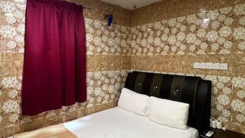 Um quarto com cama, mesa de cabeceira, janela com cortina e parede com padrão floral.