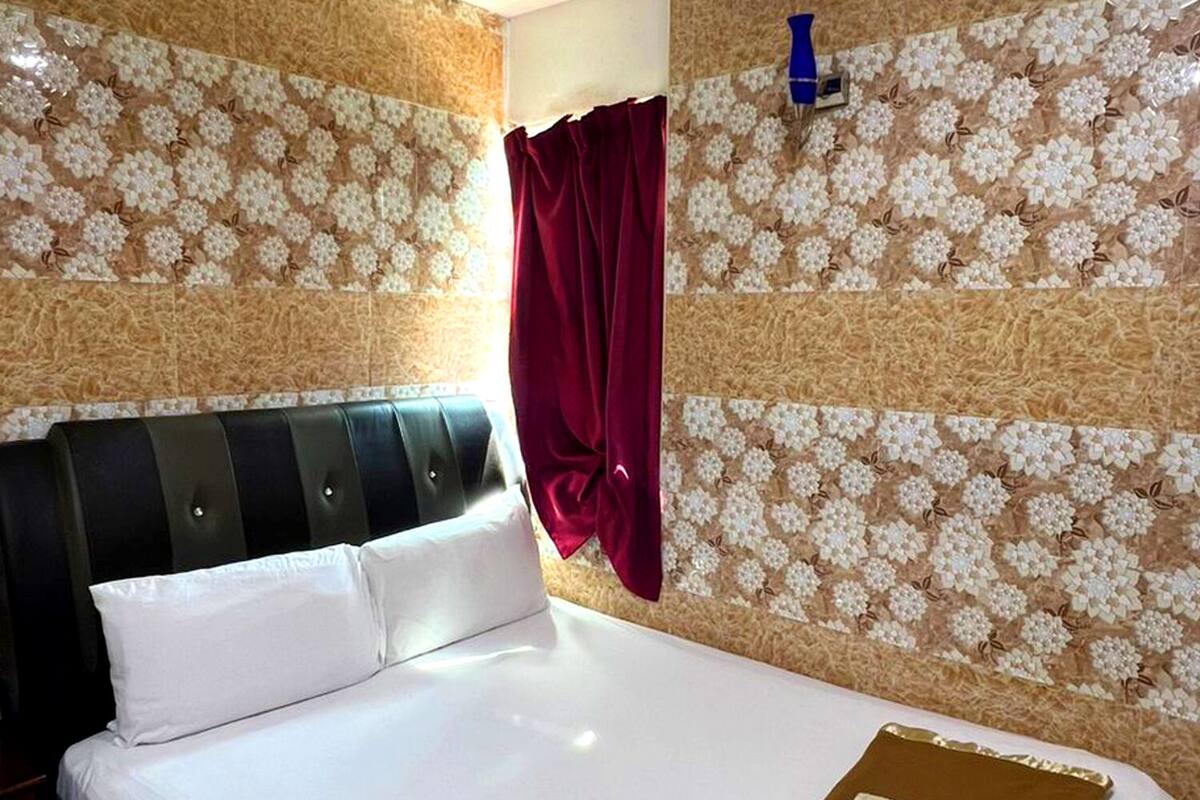 Une chambre d’hôtel avec un lit, une tête de lit, un rideau rouge et un mur orné d’un motif floral.