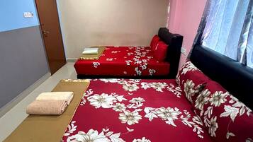 A room with two beds, each with red floral bedding and pillows, a brown mat, and a window with curtains.