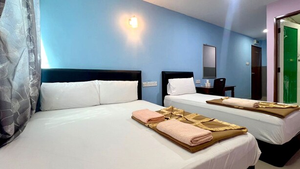 Hotelkamer met twee bedden, elk voorzien van witte lakens en handdoeken. Boven de bedden hangt een wandlamp en aan de muur is een spiegel bevestigd.