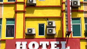 Een gebouw met een opvallend “HOTEL” bord aan de boven- en onderkant. Er zijn meerdere airconditioningunits aan de buitenmuren bevestigd.