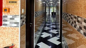 Een hotelgang met een geruit vloerkleed, een brandblusser en een rookverbods bord.