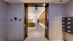 A modern elevator entrance with a digital display and a keypad, leading to a hallway with a wooden reception desk and patterned wall. - RESI STAY Kumico Amaterrace (Kyoto)