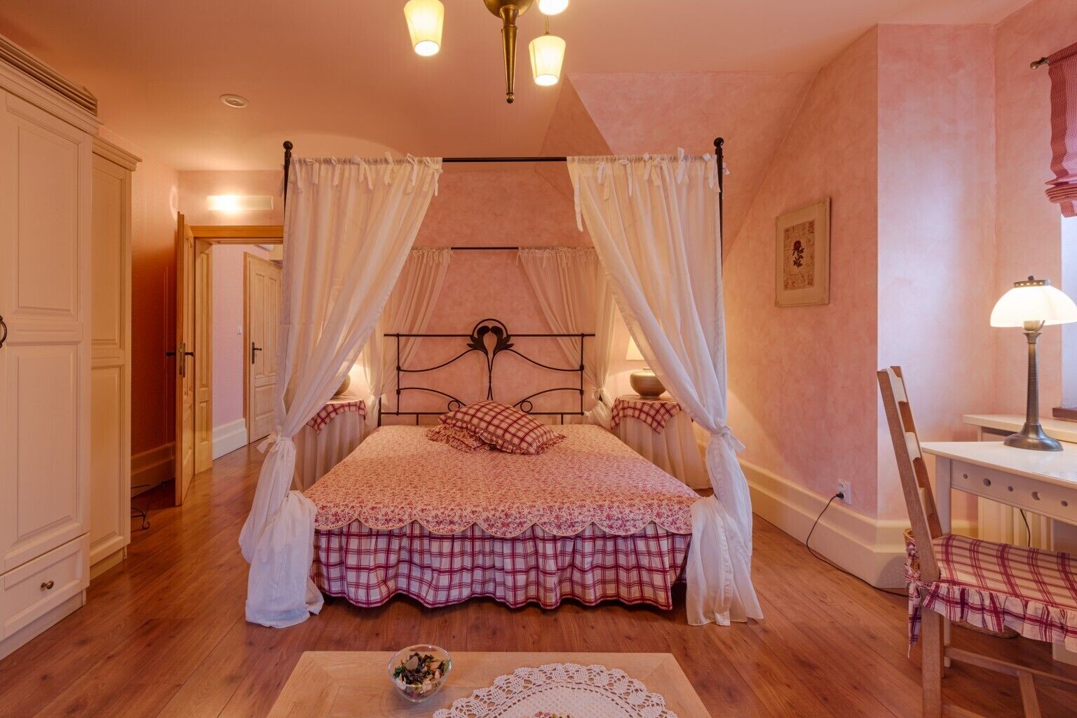 A bedroom with a four-poster bed, a bedside table with a lamp, a chair, and a small table with a bowl.