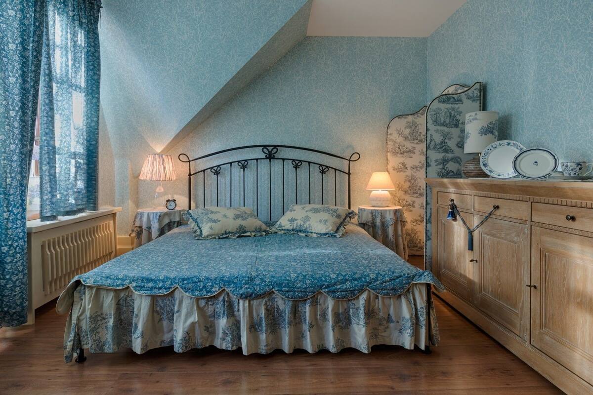 A bedroom with a bed, two bedside tables, a nightstand, a wooden cabinet, and a window with curtains.