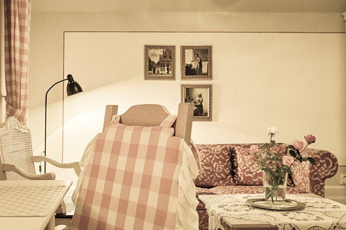 A cozy room with a checkered bed, a wicker chair, a sofa, and a table with a vase of flowers.
