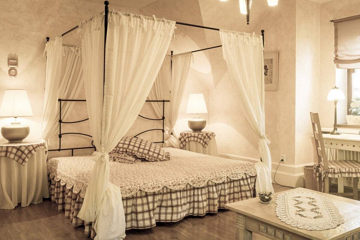 A bedroom with a four-poster bed, a desk with a chair, a radiator, and a television.