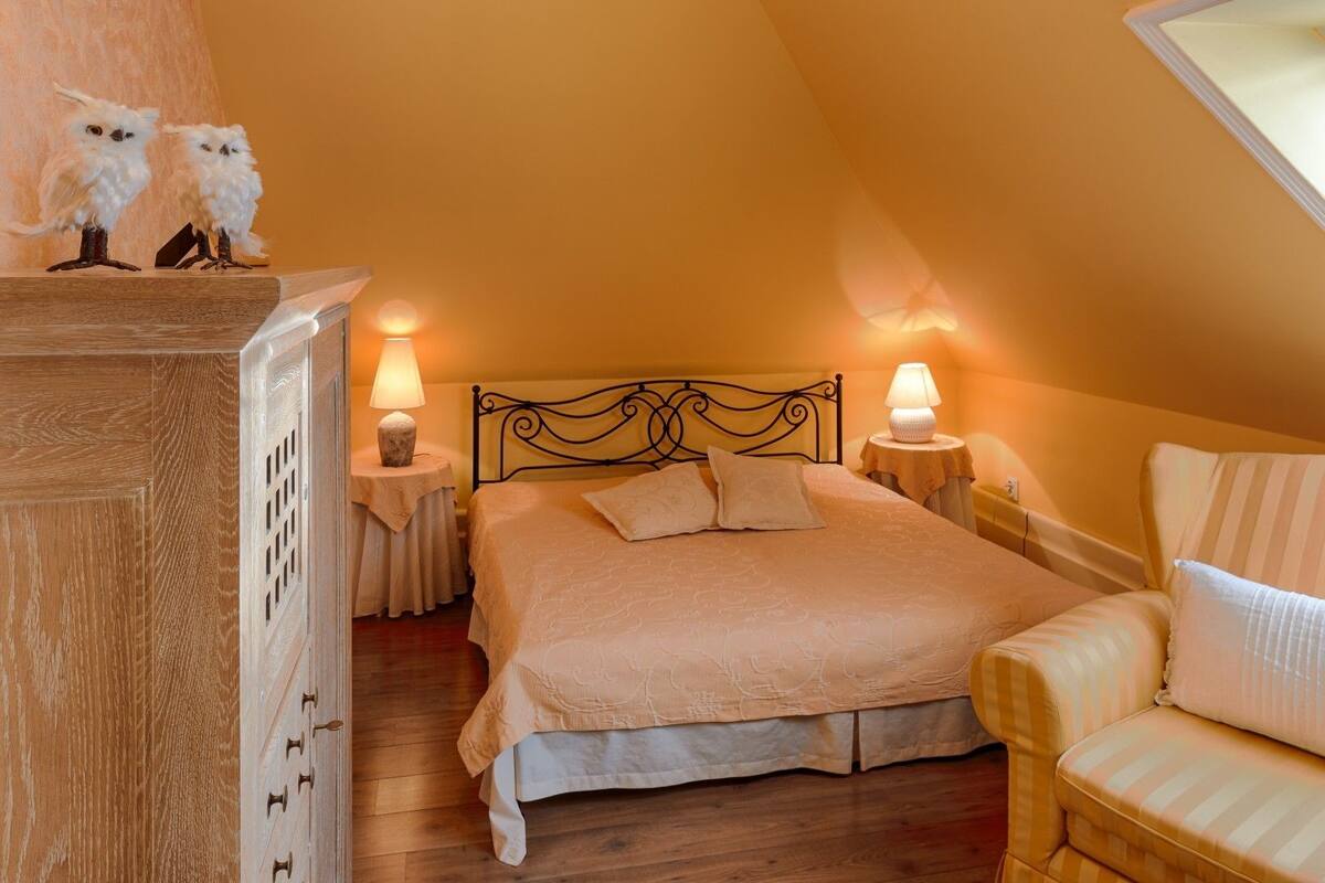 A cozy bedroom with a bed, two bedside tables with lamps, a wooden dresser, and a chair.