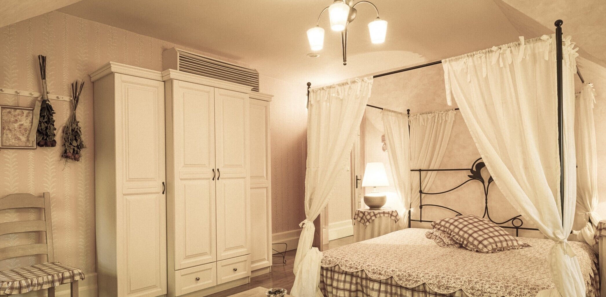 A bedroom with a canopy bed, a wardrobe, a bedside table with a lamp, and a chair.