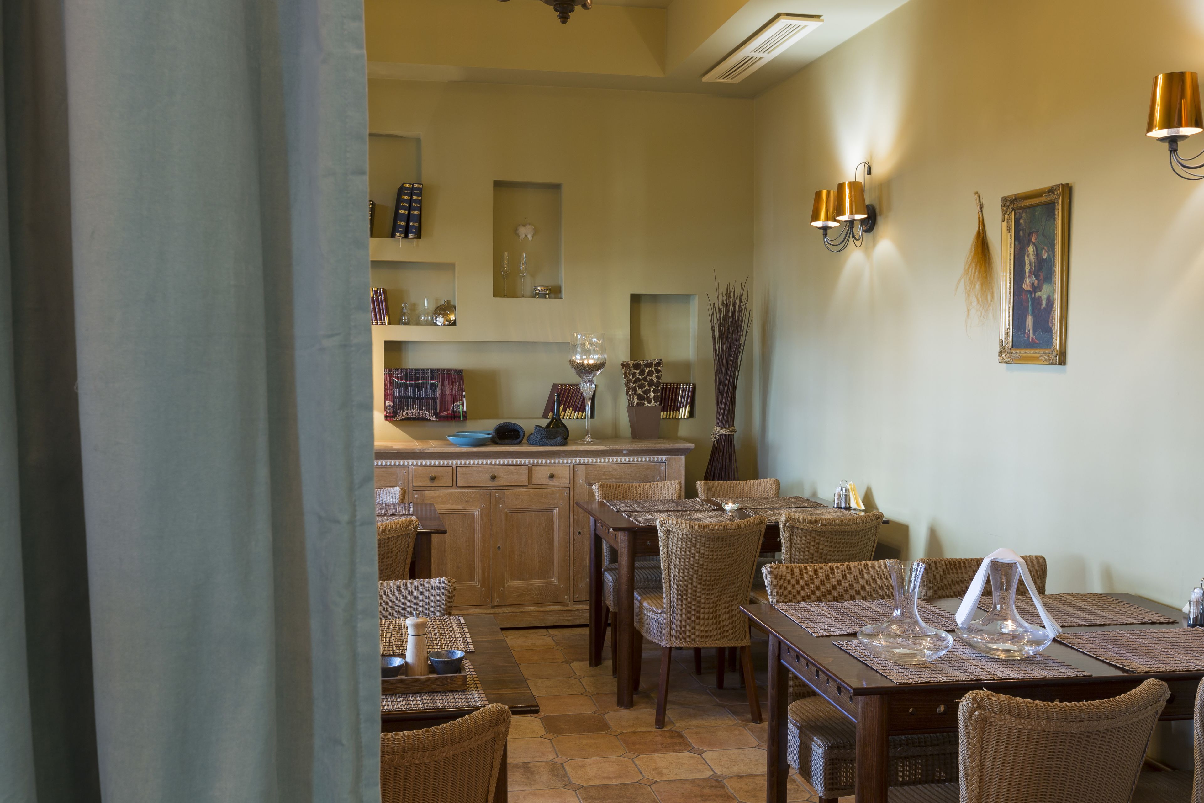 Un espace repas avec des tables et des chaises en bois, une cuisine à l’arrière-plan et des luminaires fix és au mur.