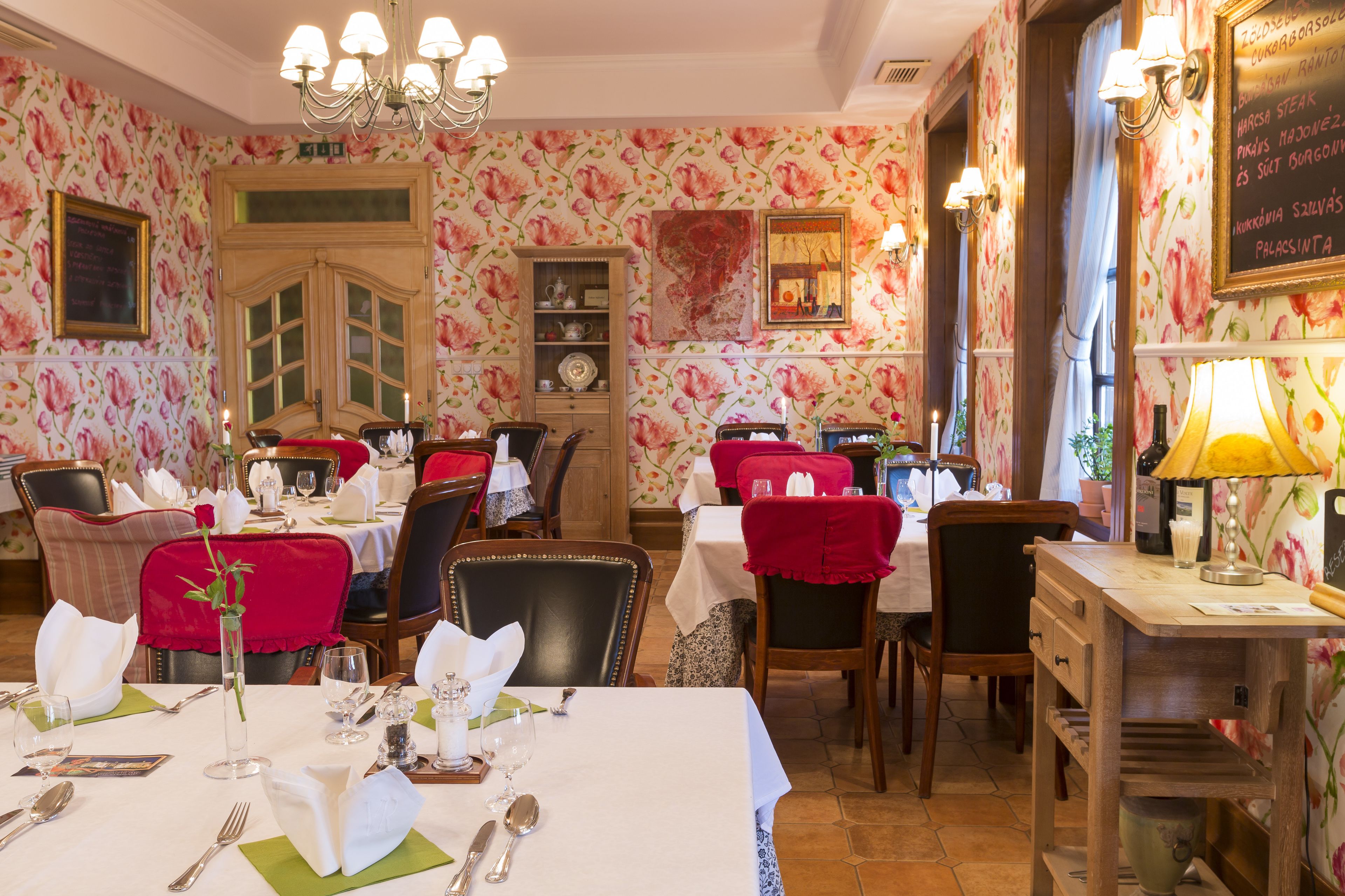 Comedor con mesas dispuestas para una comida, sillas, un candelabro y una pizarra de menú.