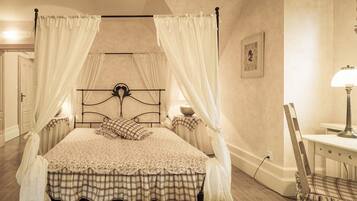 A four-poster bed with a floral bedspread and plaid skirt, a bedside table with a lamp, and a framed picture on the wall.