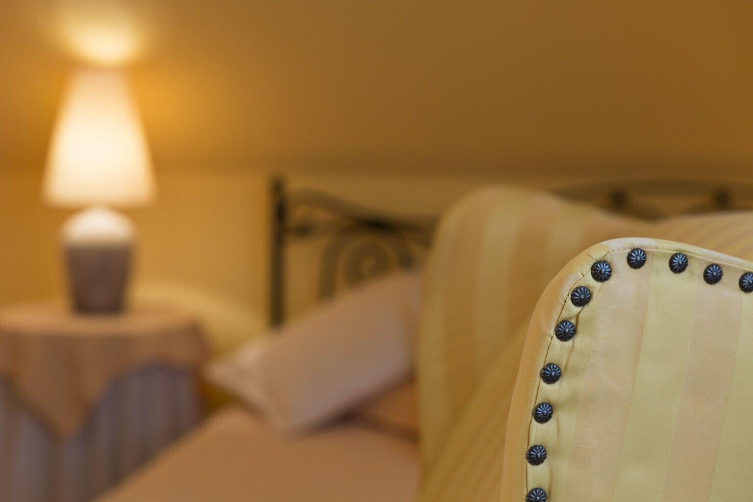 Ein Bett mit einem Kopfteil mit Zierknöpfen, einer Nachttischlampe und einem Kissen.