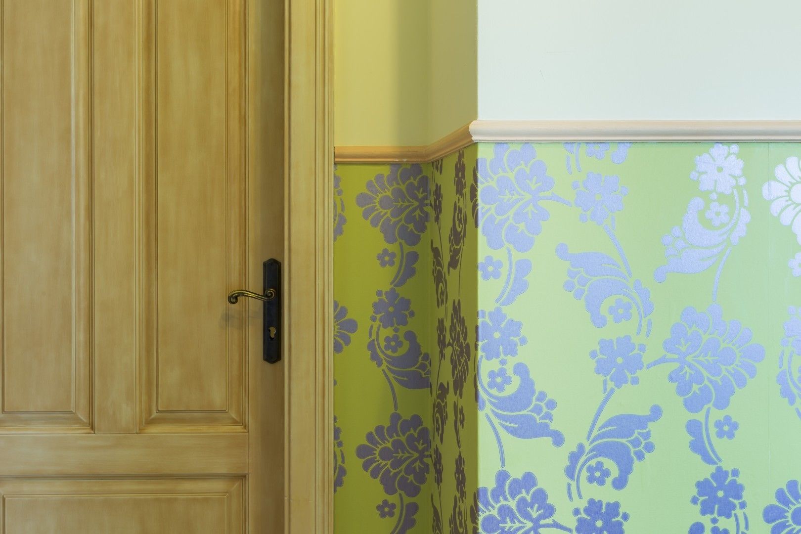 Una puerta de madera con un picaporte negro y una pared verde con diseño floral.