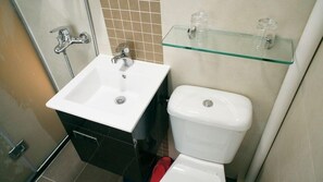 Un baño con un lavamanos blanco, un inodoro y un estante de vidrio sobre el inodoro.