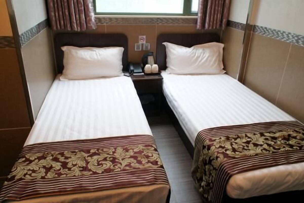 Habitación de hotel con dos camas individuales, cada una con una almohada y una mesita de noche.