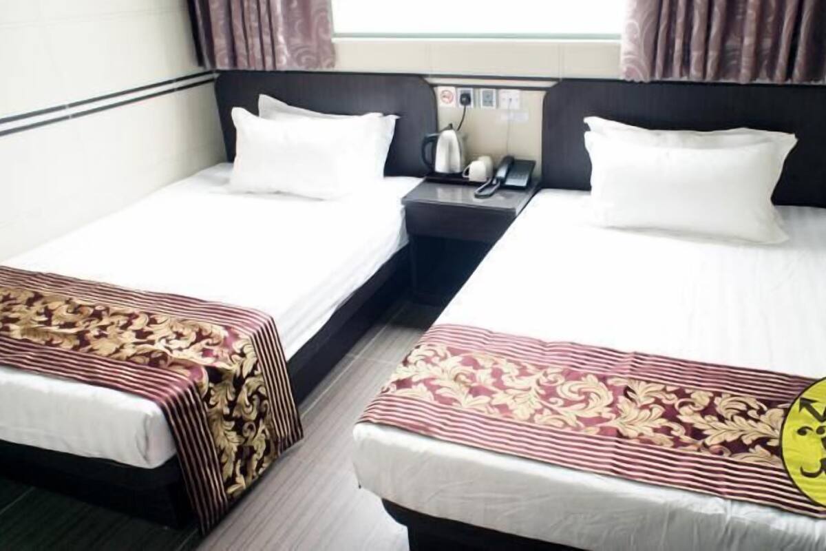 Habitación de hotel con dos camas individuales, una mesita de noche con teléfono y hervidor, y una ventana con cortinas.