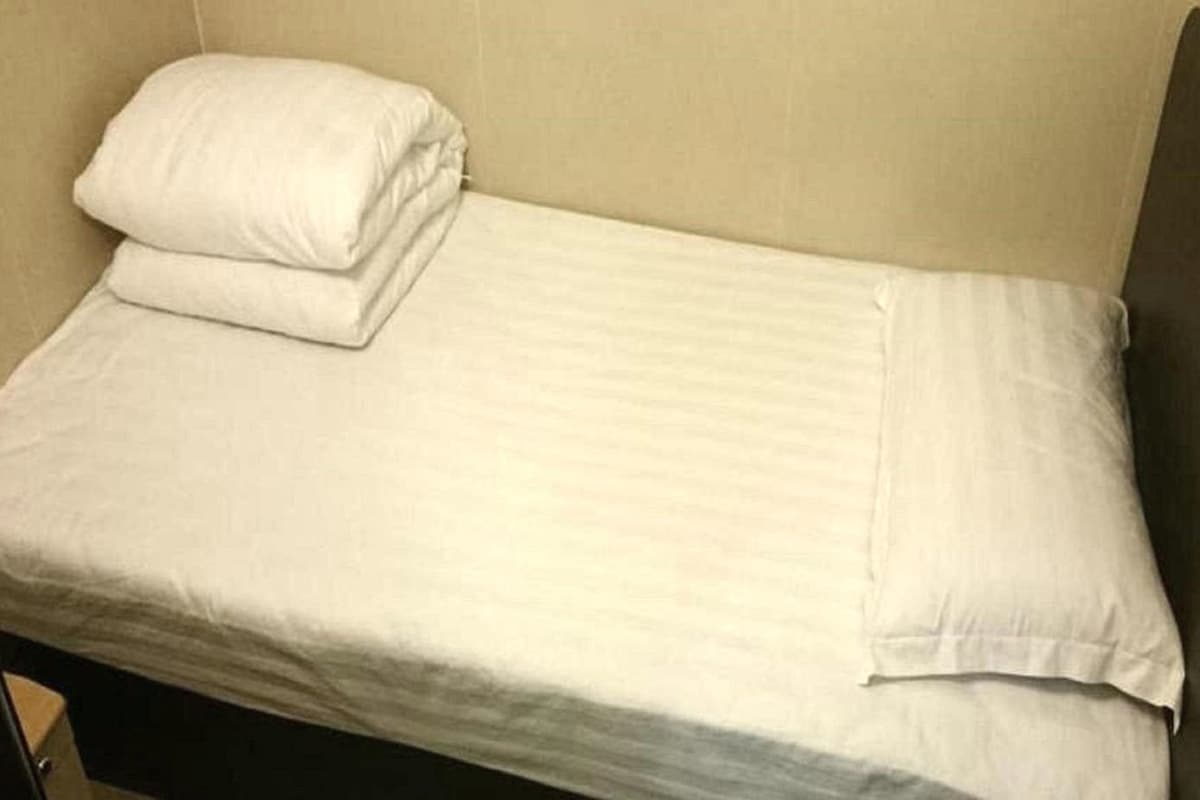 A single bed with white linens in a room with a plain wall and a dark floor.