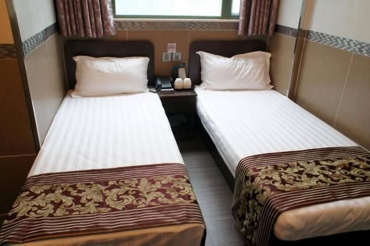 Habitación de hotel con dos camas individuales, una mesita de noche, un teléfono y una ventana con cortinas.