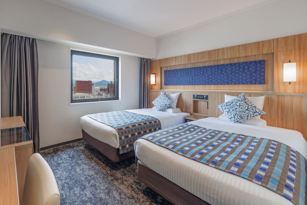 Une chambre d’hôtel avec deux lits, un bureau, une télévision et une fenêtre donnant sur la ville.