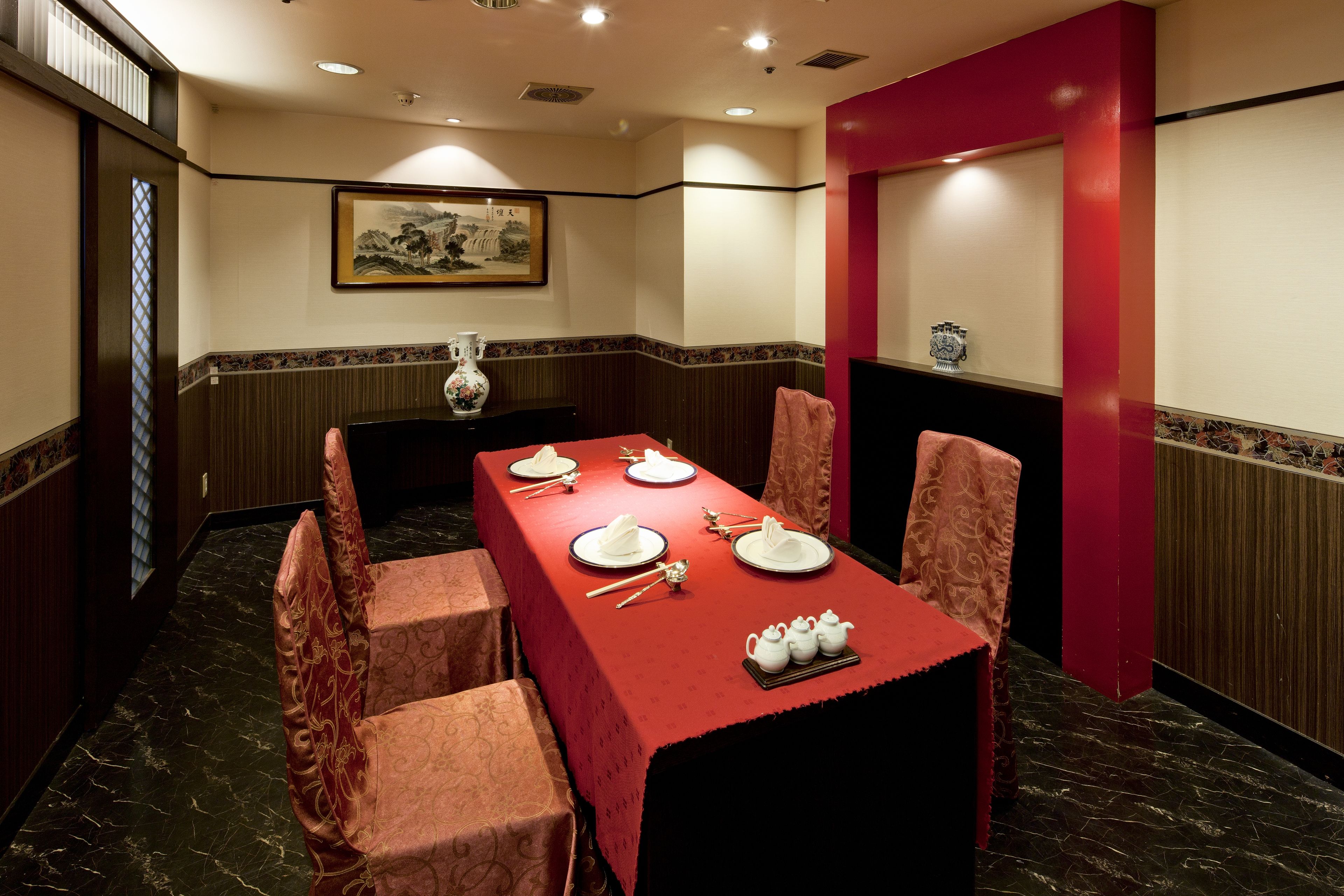 A conference room with a long table set for four, surrounded by chairs, a vase, and teapots.