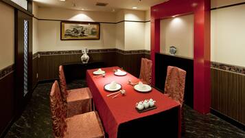 A conference room with a long table set for four, surrounded by chairs, a vase, and teapots.