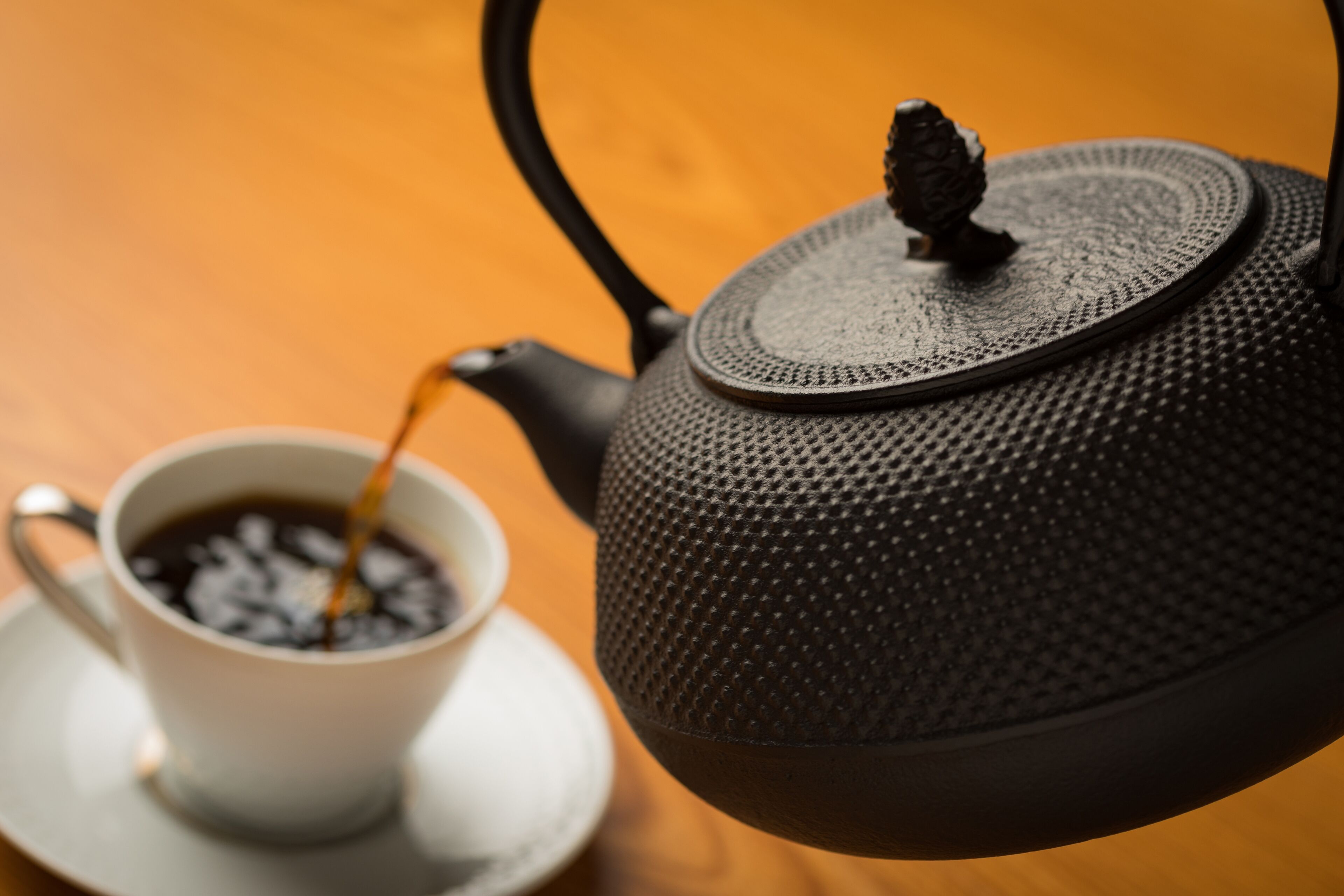 Una tetera con superficie texturizada y un asa, colocada junto a una taza de café sobre un platito.