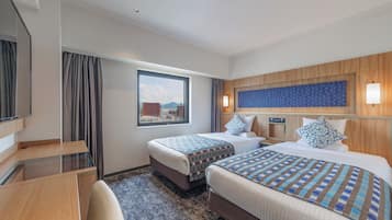 A hotel room with two beds, a desk, a chair, a window with curtains, and a city view.