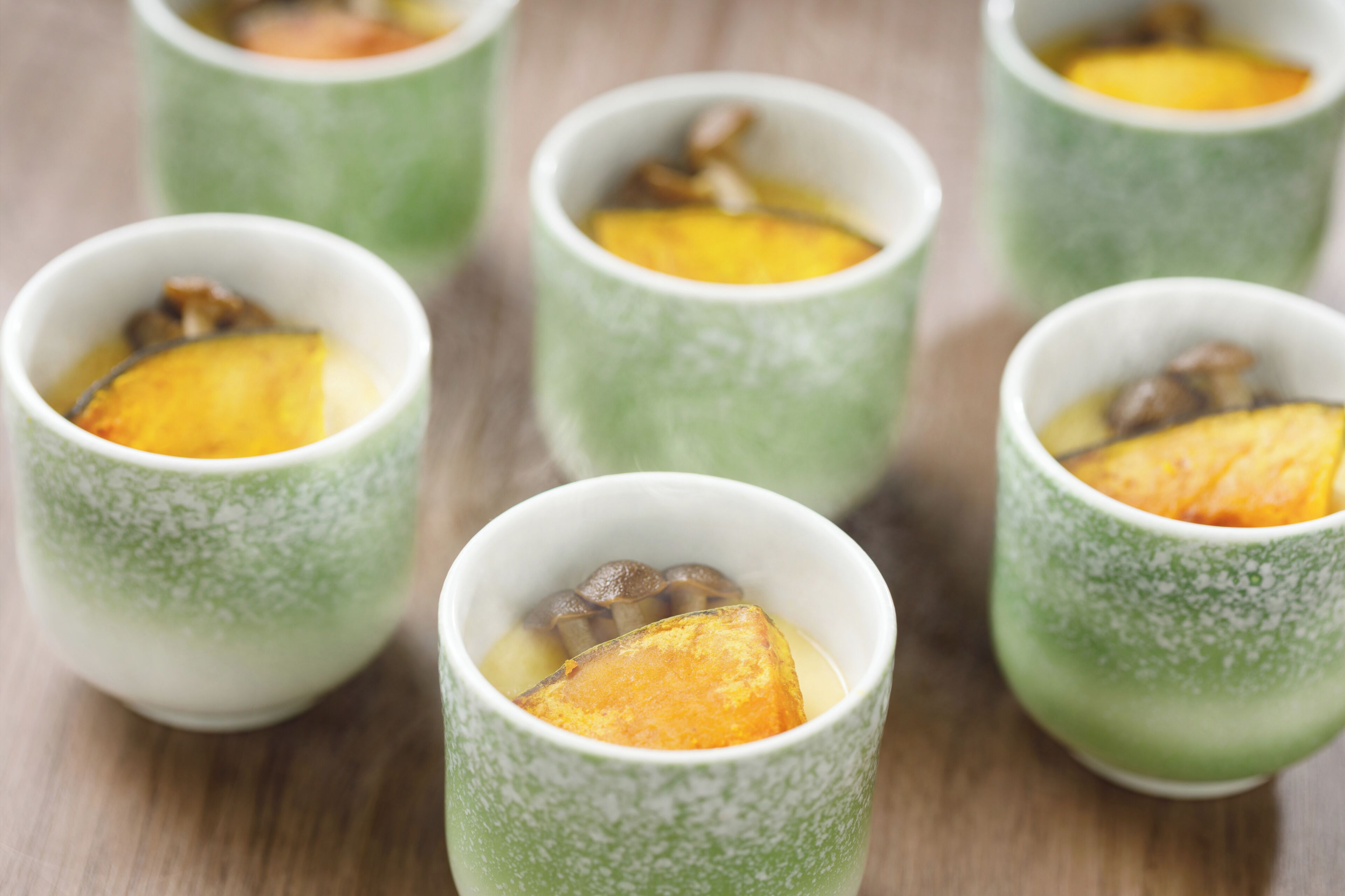 A series of green cups with a textured pattern, each containing a slice of yellow fruit and some brown items, possibly mushrooms, on a wooden surface.