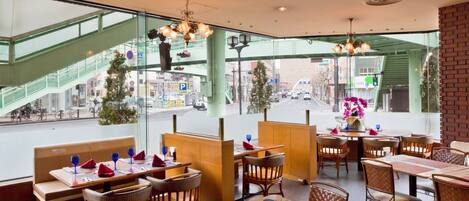 Un restaurant avec des tables et des chaises, une vue sur la rue et un escalier en arrière-plan.