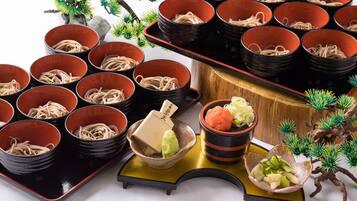 A traditional Japanese meal setup with multiple bowls of noodles, a small dish of wasabi, and a decorative bonsai tree.