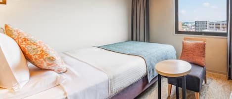 A hotel room with a bed, a small round table, a chair, and a window with a city view.