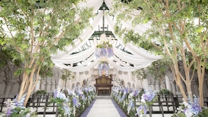 An indoor venue with a central aisle, flanked by trees and draped fabric, leading to a stage with an organ. - ART HOTEL Morioka (Morioka)