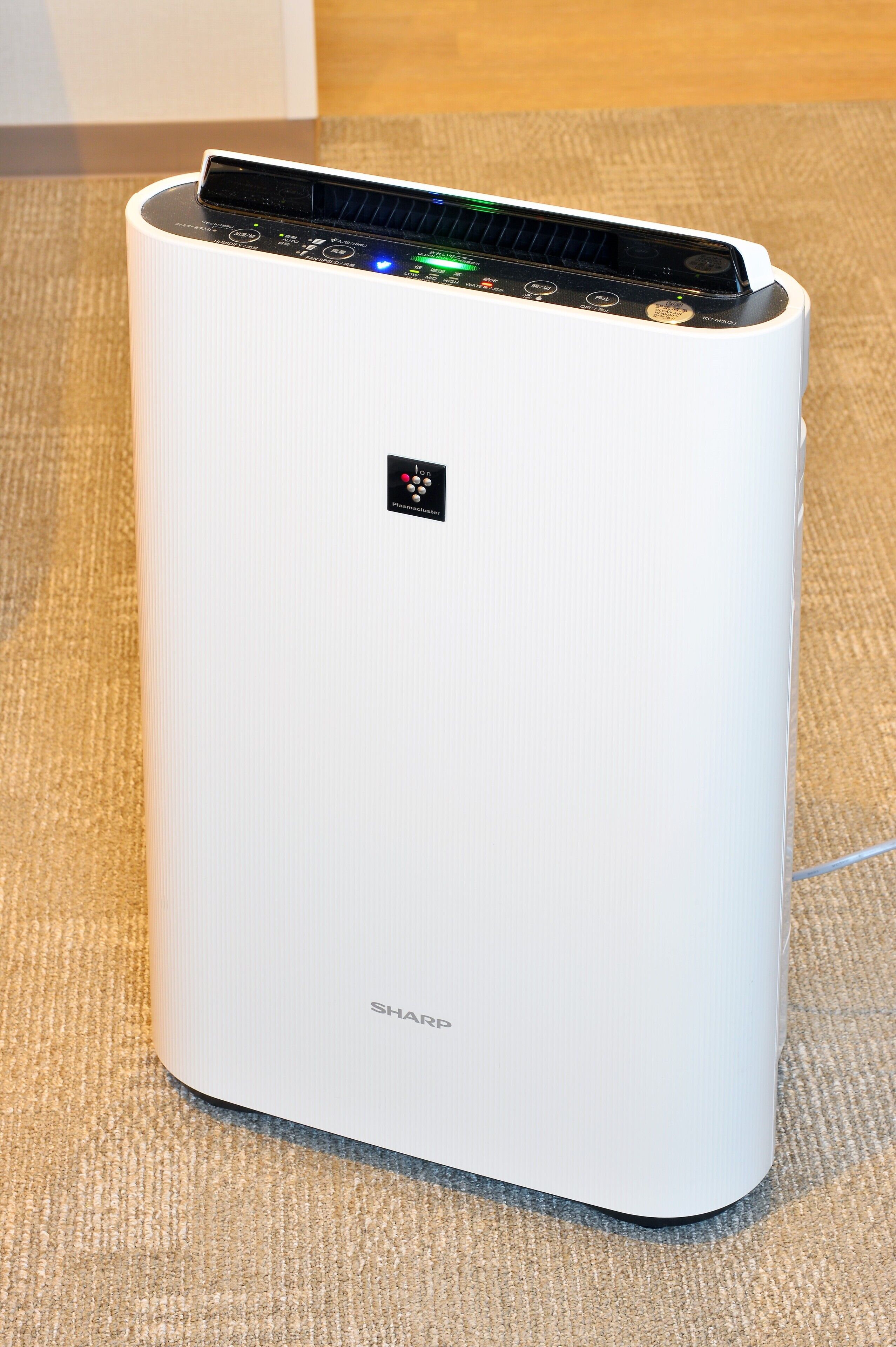 A white, modern air purifier with a control panel and a small logo on the top.