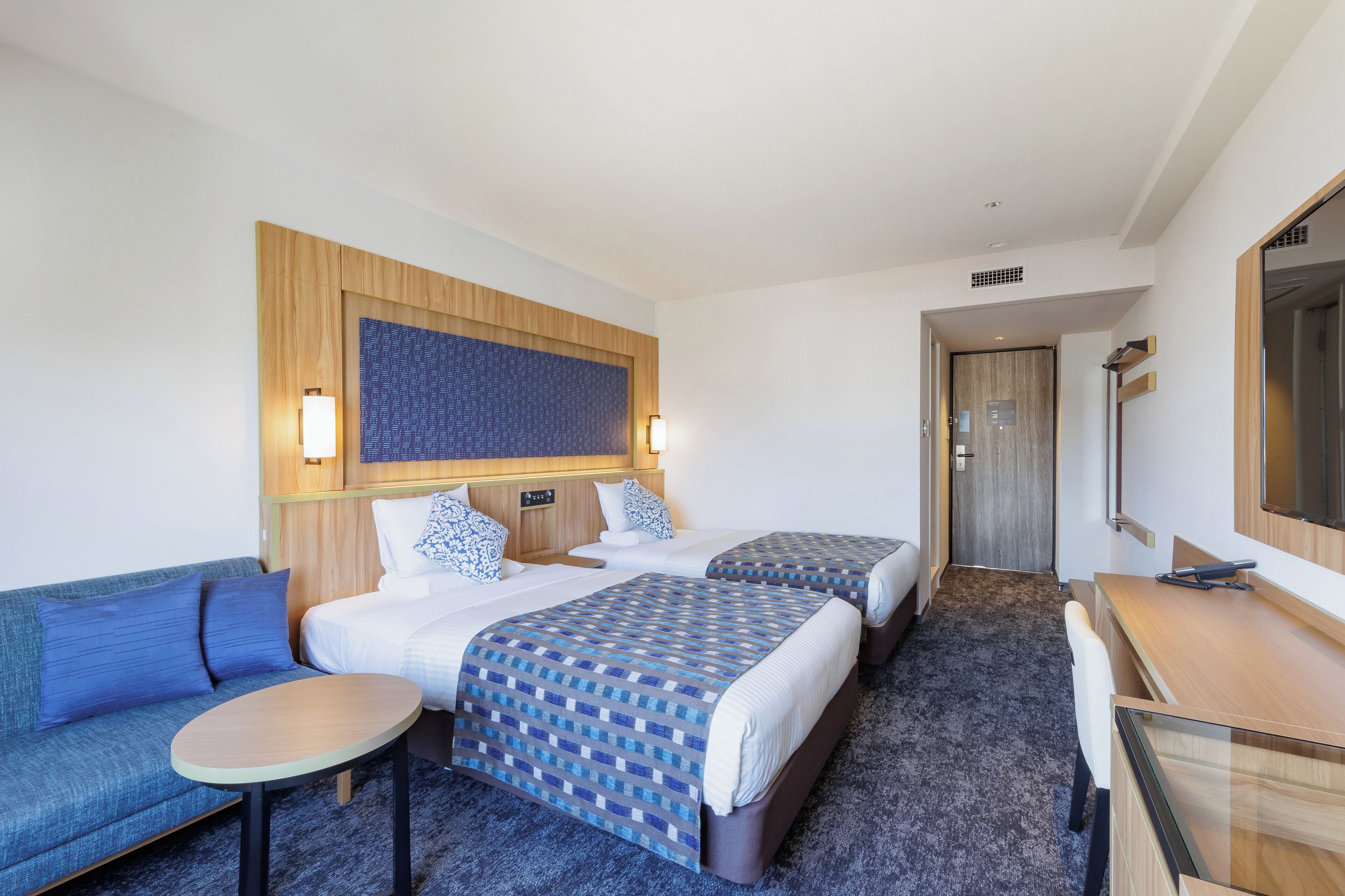 Ett hotellrum med två sängar, en soffa, ett skrivbord och en spegel.