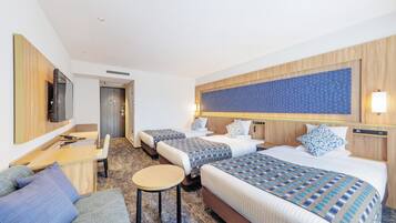 Quarto de hotel com duas camas, um sofá, uma mesinha, uma TV e uma obra de arte na parede.