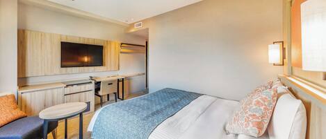 A hotel room with a bed, a desk, a chair, a television, and a lamp.