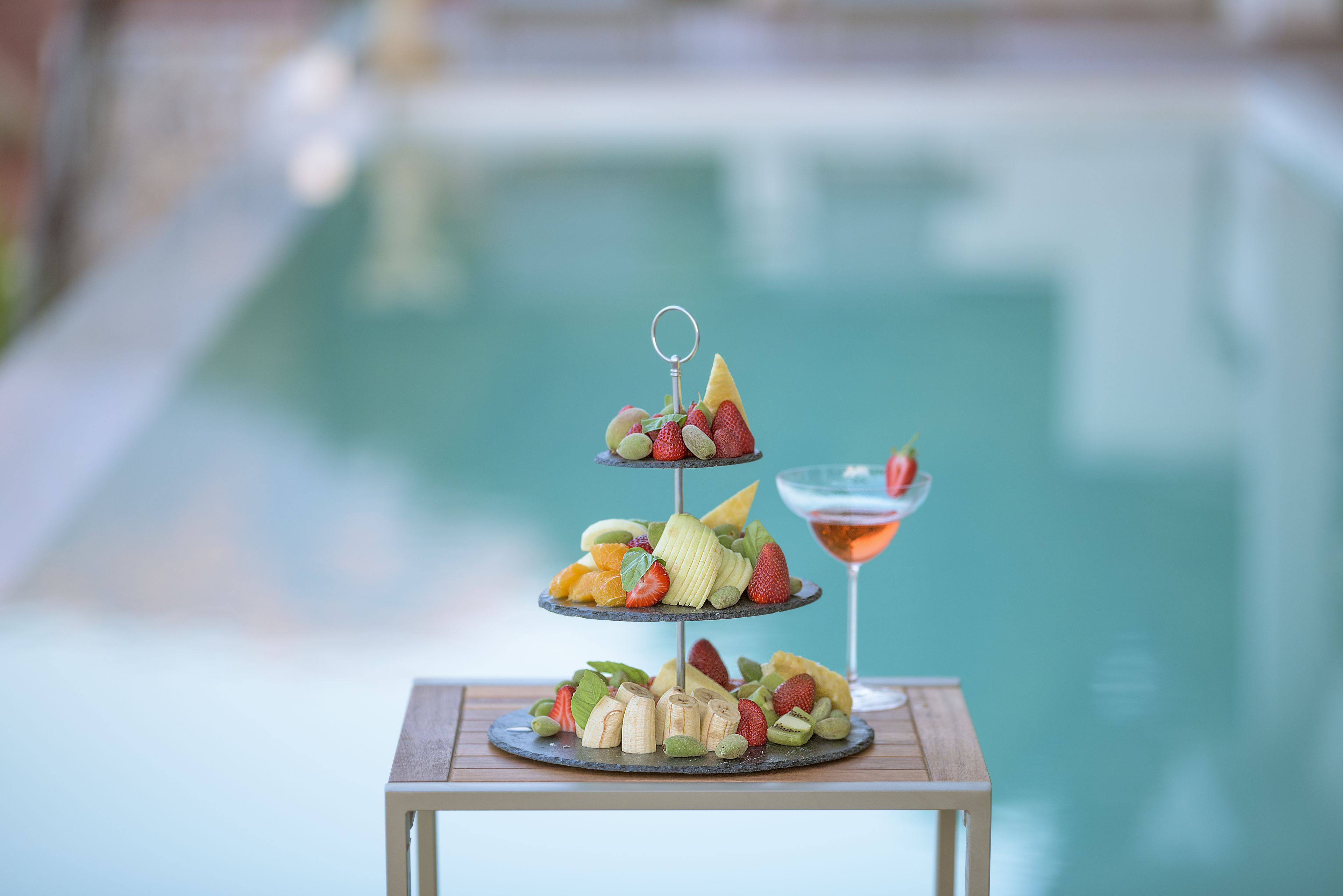 A three-tiered fruit platter on a table by a poolside.