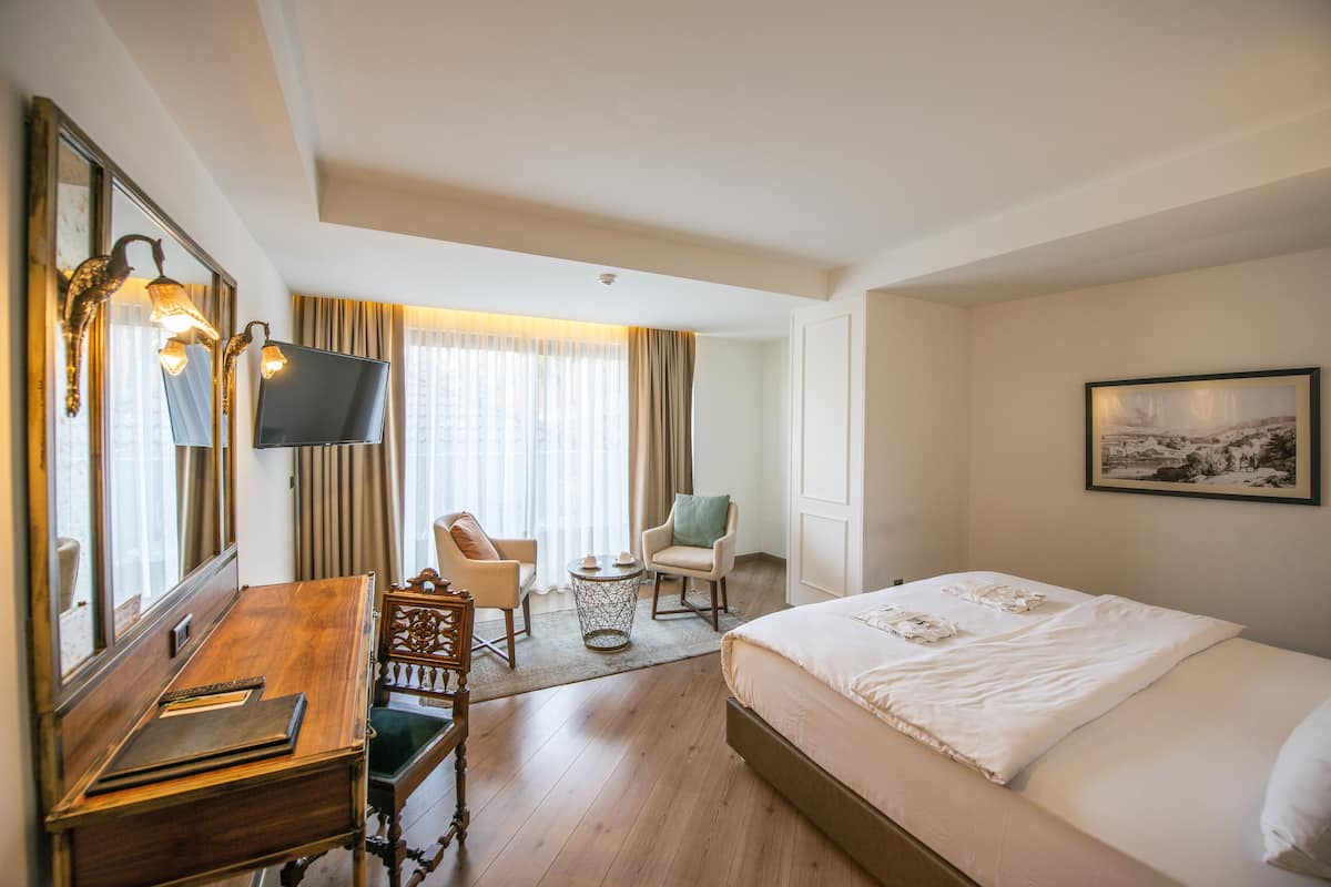 A hotel room with a large bed, a desk with a chair, a television, and a window with curtains.