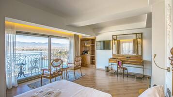 A hotel room with a large bed, a desk, a chair, a wardrobe, and a balcony with a view of the mountains.