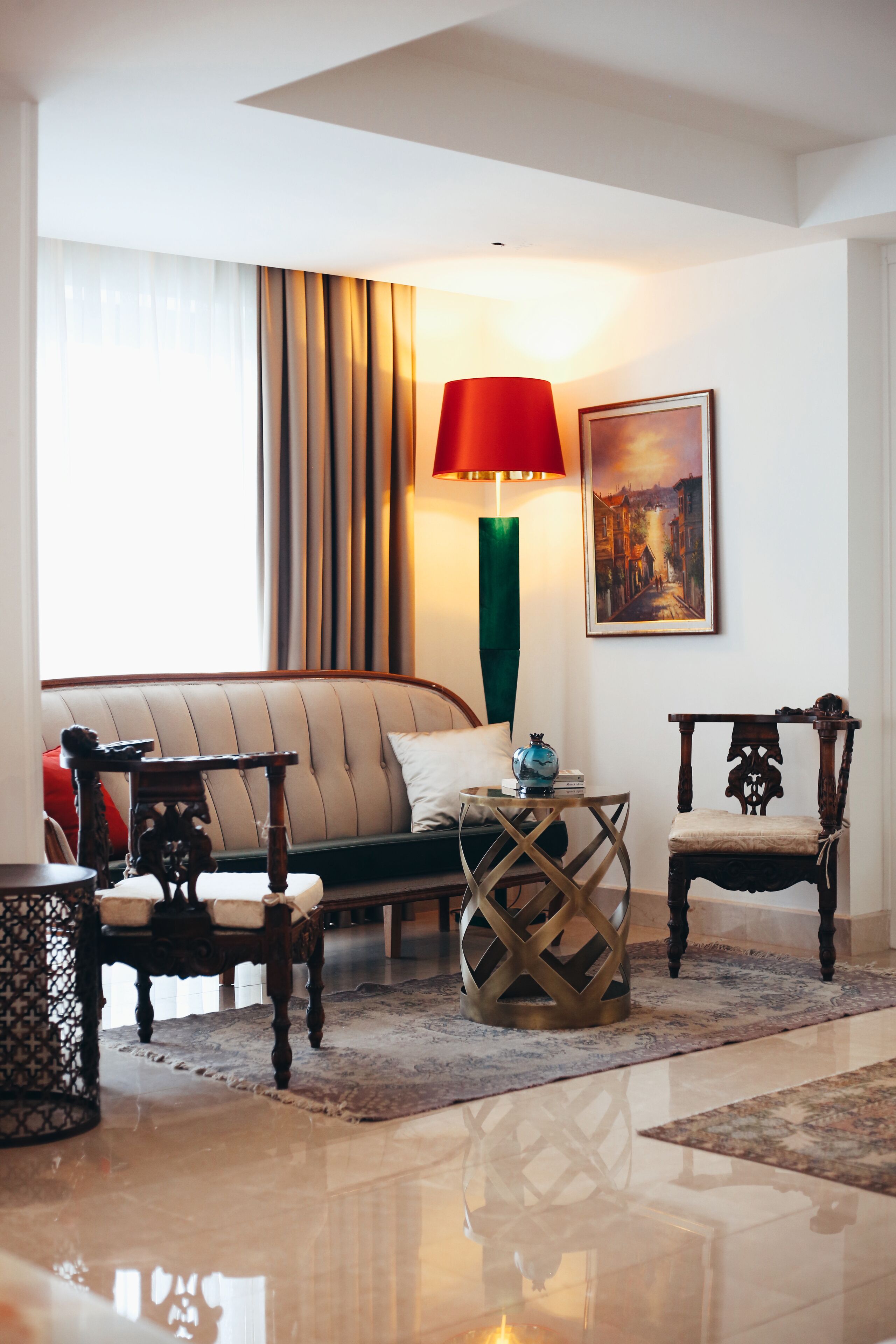A well-lit living room with a sofa, two chairs, a table with a lamp, and a painting on the wall.