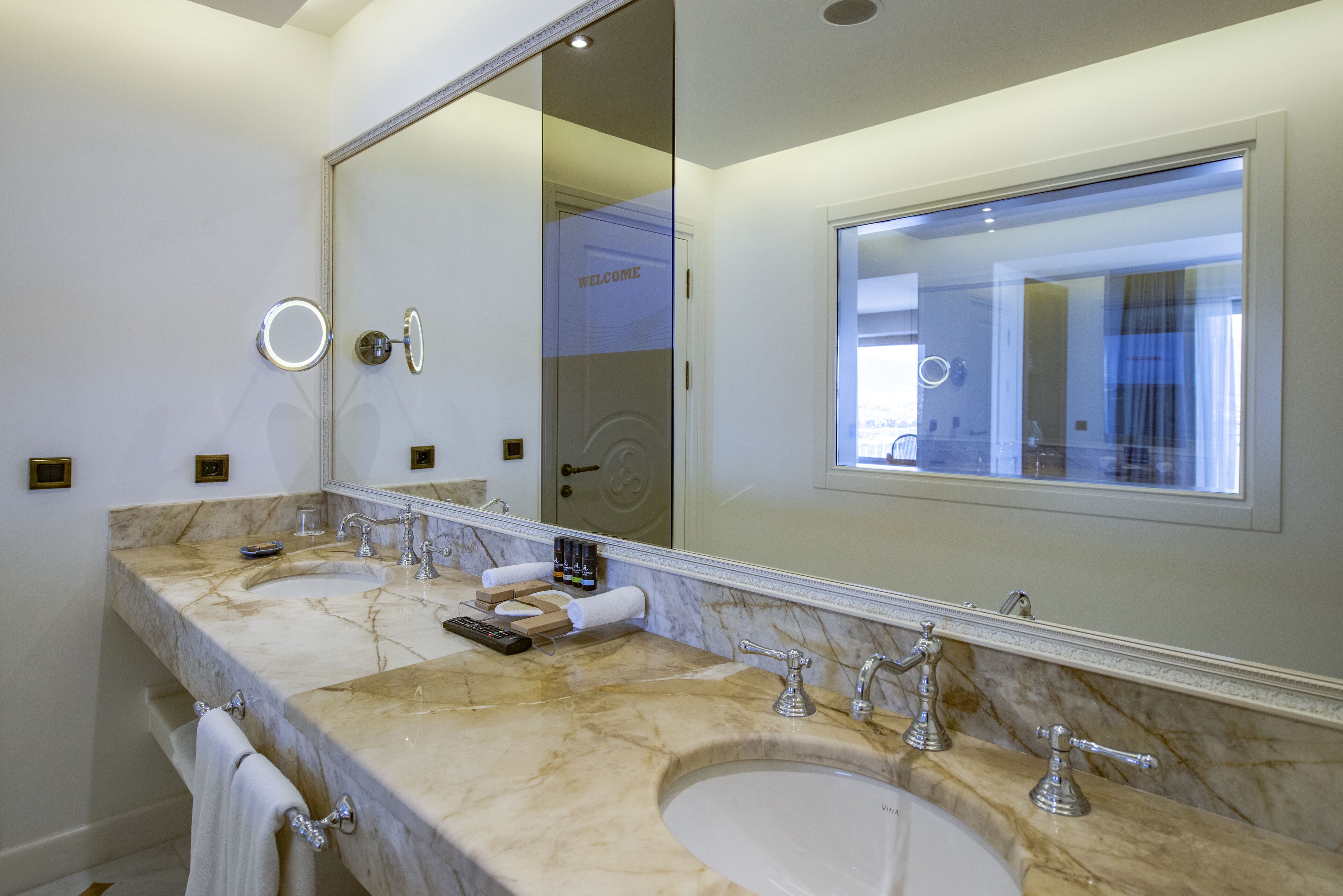 Un baño moderno con dos lavamanos, un espejo grande y un cartel que dice 'WELCOME'.