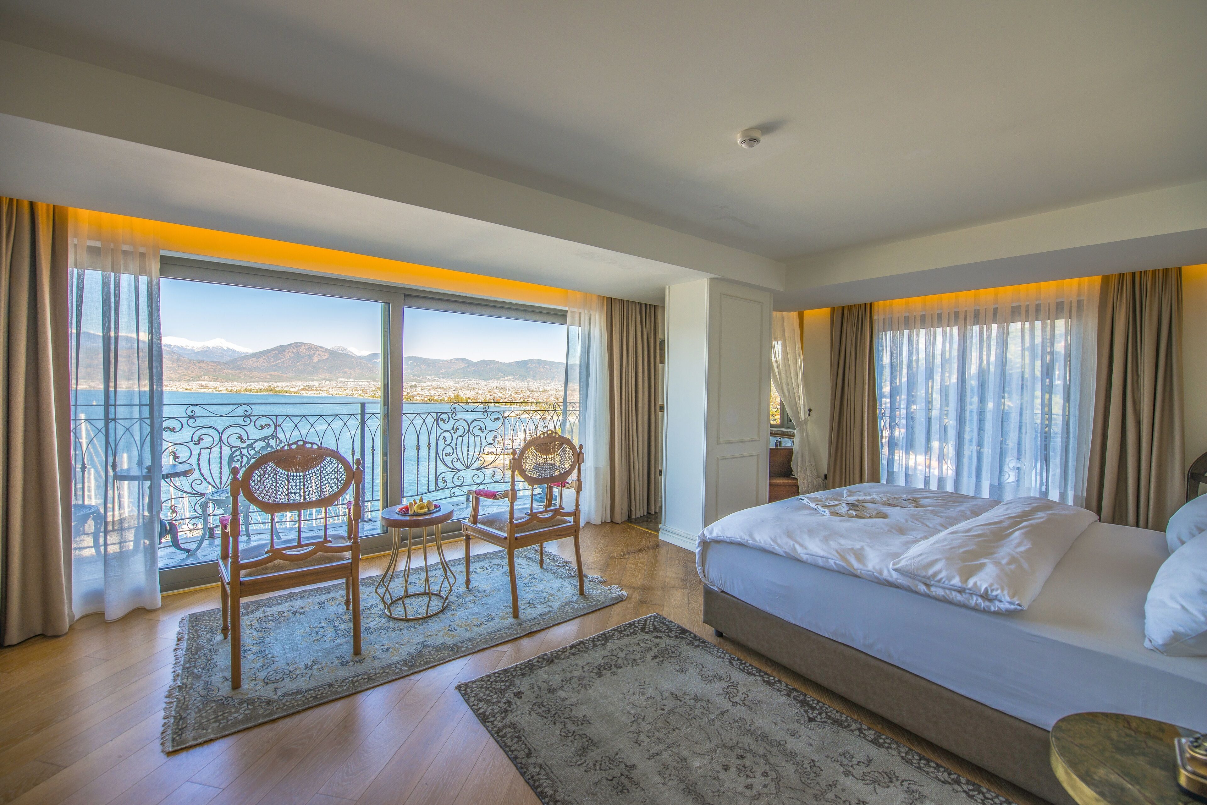 A bedroom with a large bed, a balcony with a view of mountains, and a dining area with chairs and a table.