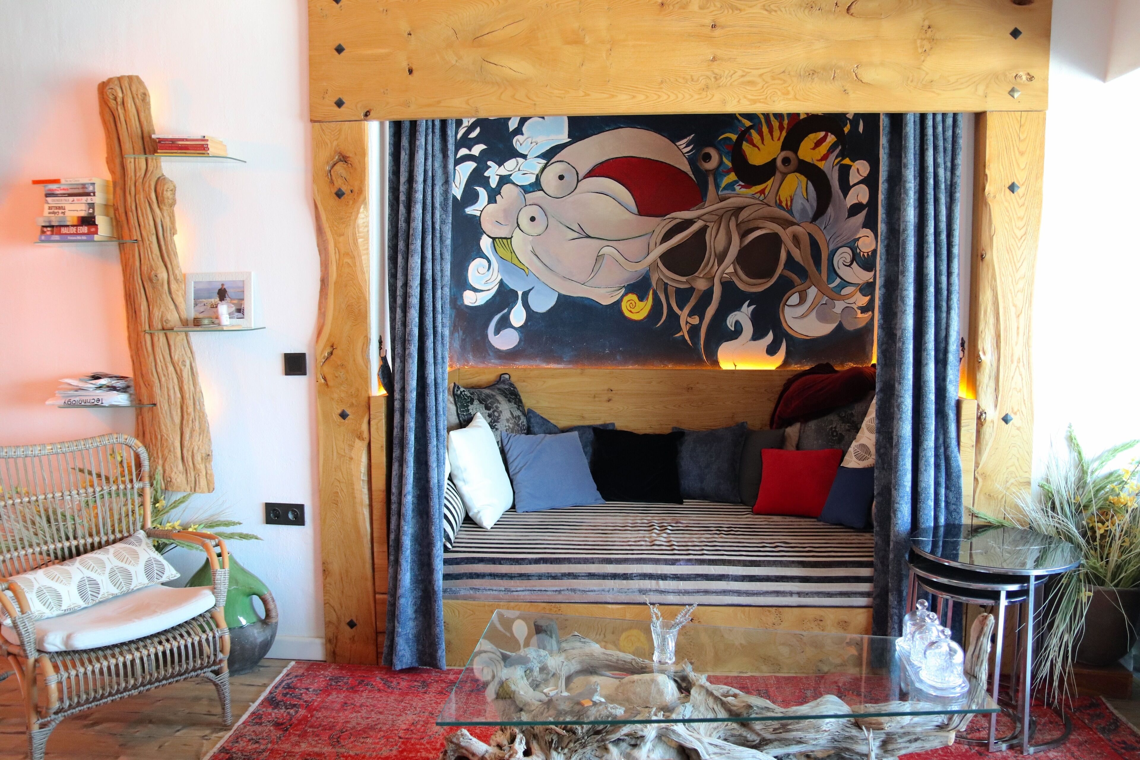 A cozy room with a bed, a wicker chair, a glass coffee table, and a wall mural.