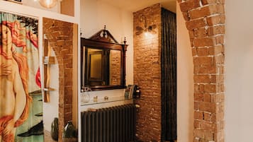 A bathroom with a brick wall, a mirror, a radiator, and a glass shelf with toiletries.