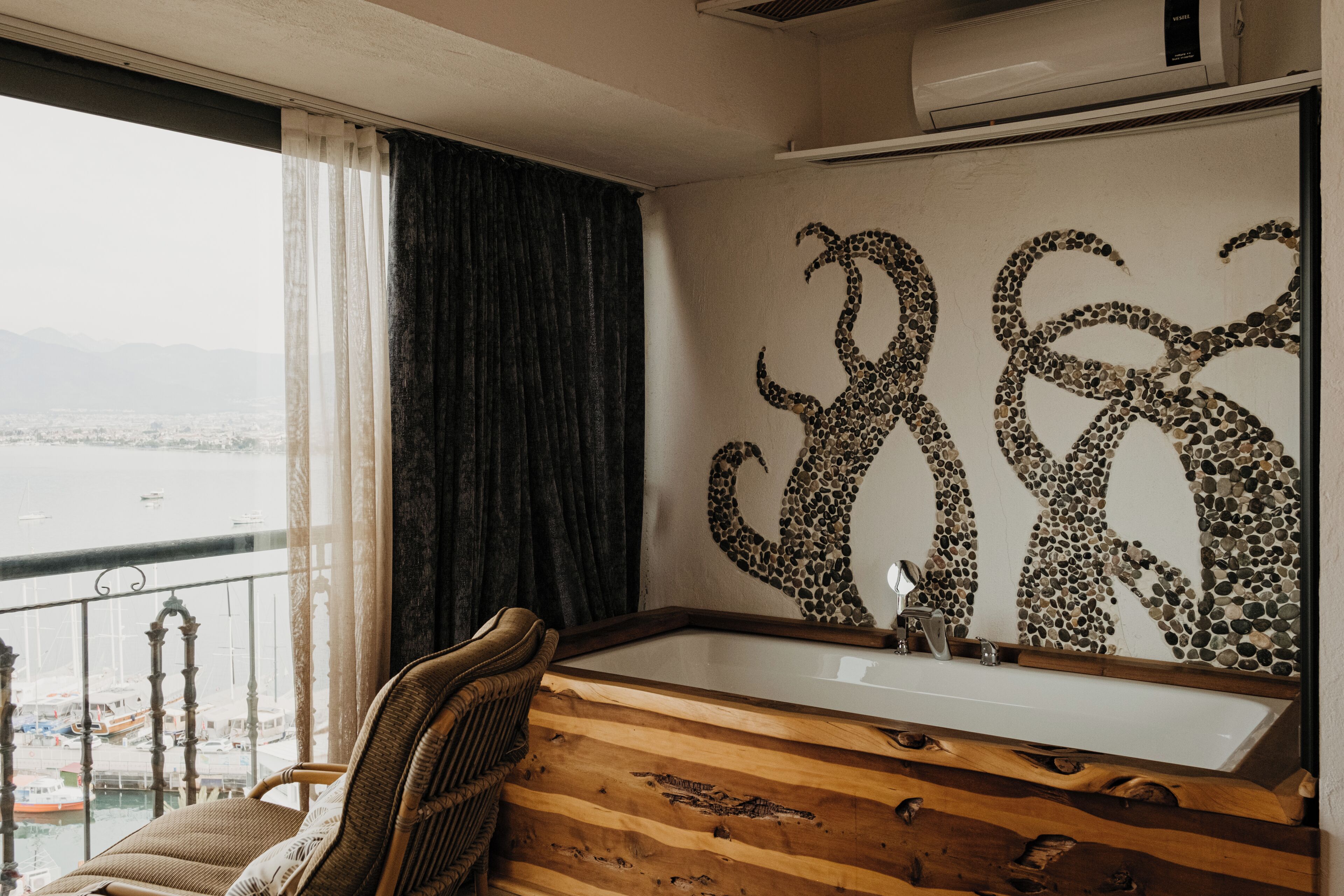 A room with a wooden vanity, a bathtub, and a large window overlooking a body of water.