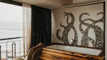 A room with a wooden vanity, a bathtub, and a large window overlooking a body of water.