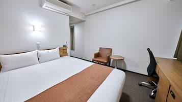 Ein Hotelzimmer mit einem großen Bett, einem Schreibtisch, einem Stuhl, einem kleinen runden Tisch und einer Klimaanlage.